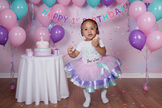 Child wearing a festive outfit with a purple and green skirt, holding a piece of cake.