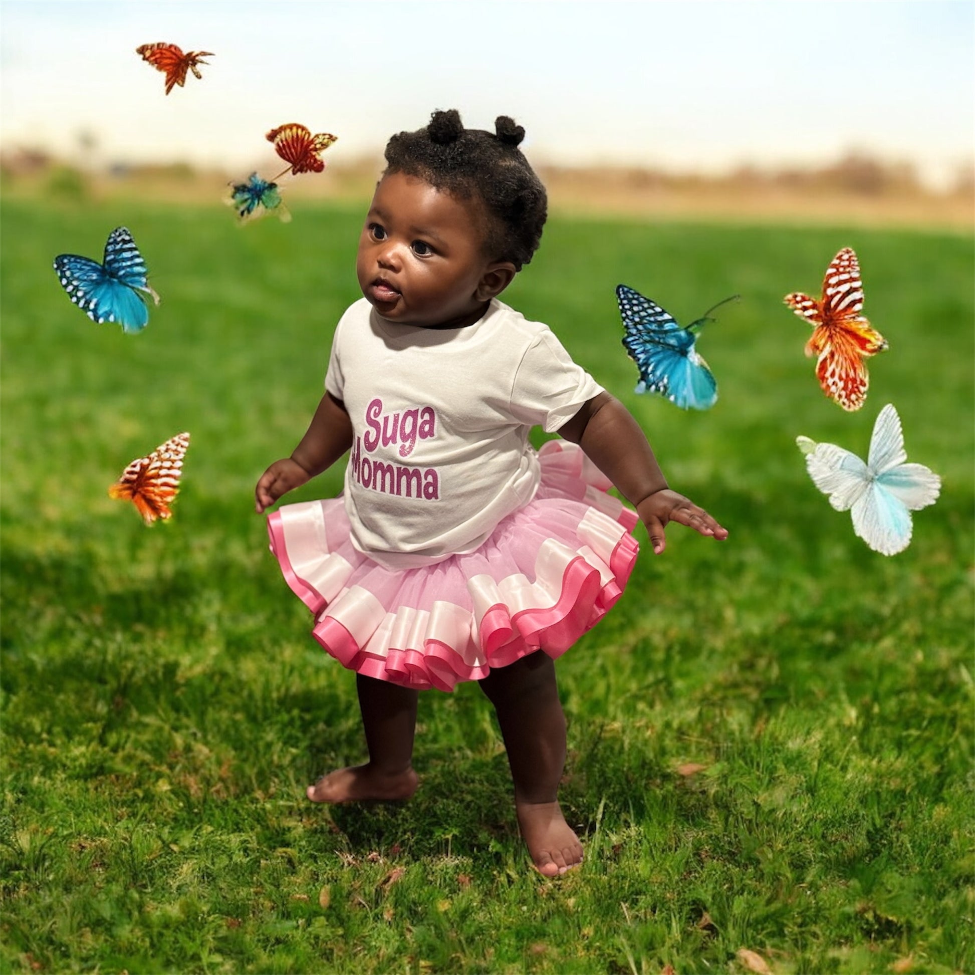 Child in a white shirt with 'Suga momma' text and pink skirt standing on grass with butterflies around.