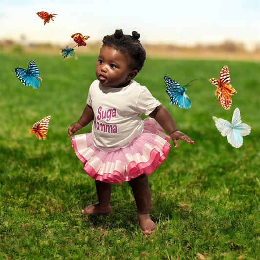 Child in a white shirt with 'Suga momma' text and pink skirt standing on grass with butterflies around.